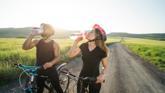 man and woman outside on bicycles drinking water