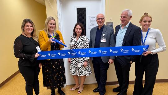 6 people stand together to cut a Catholic Ribbon