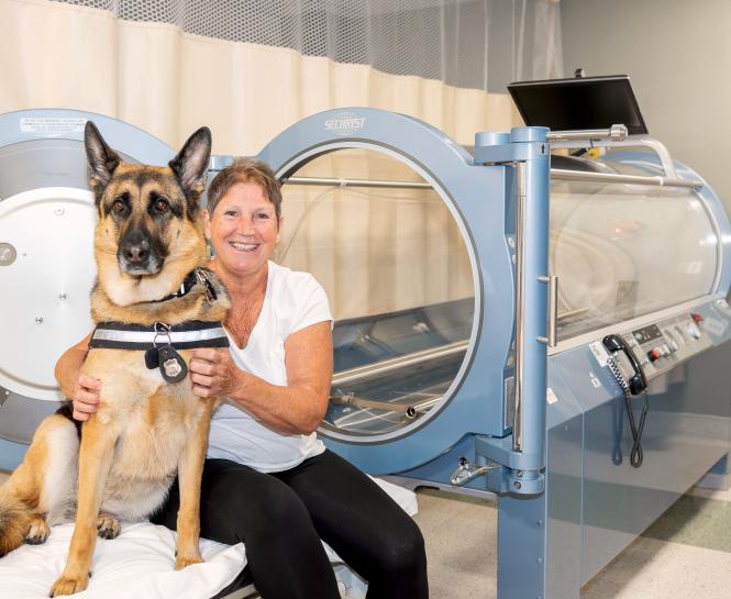 Patient sits in front of the hyperbaric oxygen chamber with her german shepherd