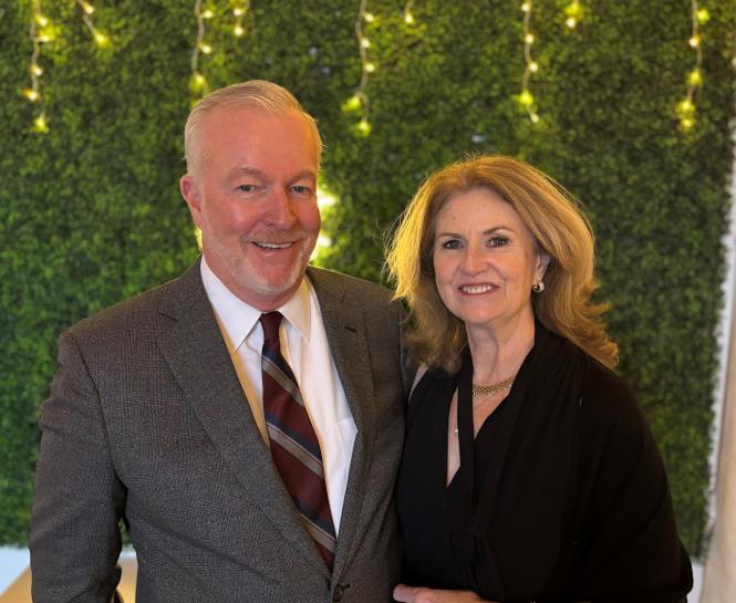 Bob and Cathy Creighton stand in front of an ivy wall with string lights