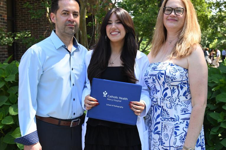 Student stands between two adults and holds diploma at the Mercy Hospital School of Radiology Graduation